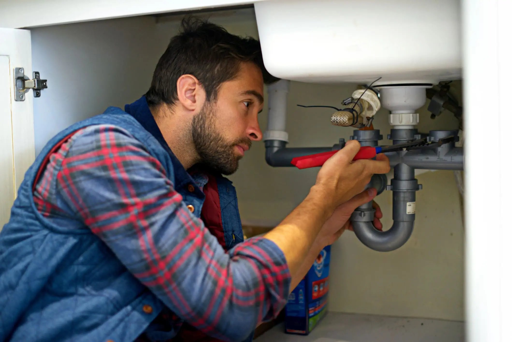 Professional plumber repairing pipes under a kitchen sink
